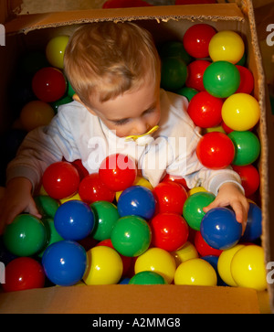 baby sitting in box with hundreds of colorful plastic balls Stock Photo