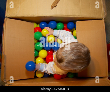 baby sitting in box with hundreds of colorful plastic balls Stock Photo