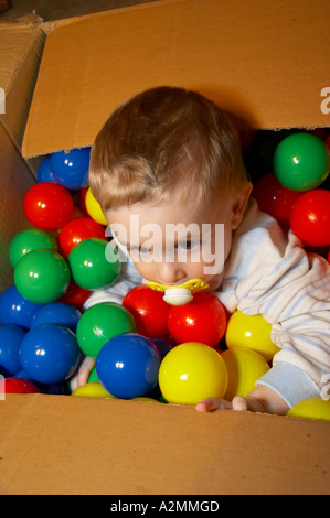 baby sitting in box with hundreds of colorful plastic balls Stock Photo