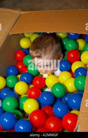 baby sitting in box with hundreds of colorful plastic balls Stock Photo