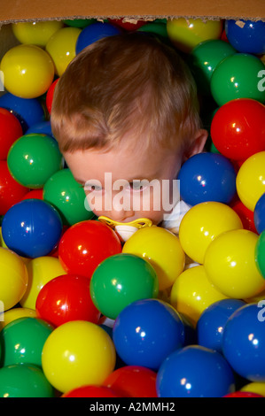 baby sitting in box with hundreds of colorful plastic balls Stock Photo