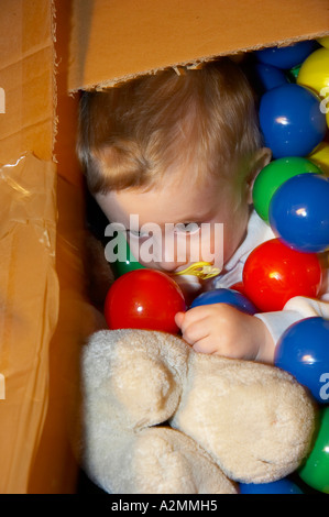 baby sitting in box with hundreds of colorful plastic balls Stock Photo