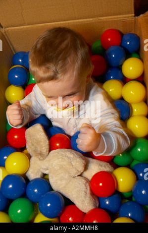 baby sitting in box with hundreds of colorful plastic balls Stock Photo