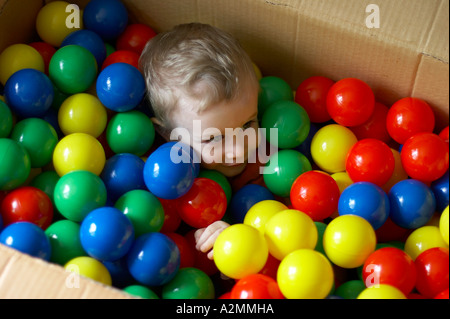 baby sitting in box with hundreds of colorful plastic balls Stock Photo