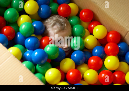 baby sitting in box with hundreds of colorful plastic balls Stock Photo