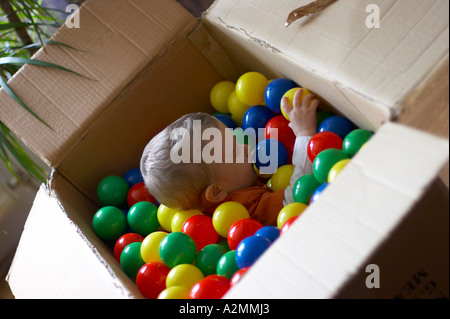 baby sitting in box with hundreds of colorful plastic balls Stock Photo