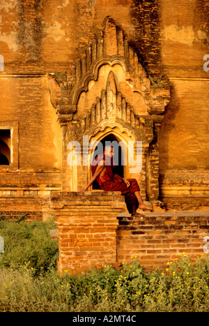 Burmese monk in traditional red robes sits outside the  mellow Mingun pagoda in Pagan(Bagan),Myanmar Stock Photo