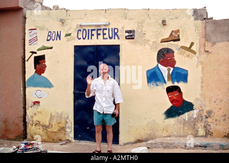 A man with a shaved head gives the 'OK' sign outside a barbers shop in Mali, west Africa. Stock Photo