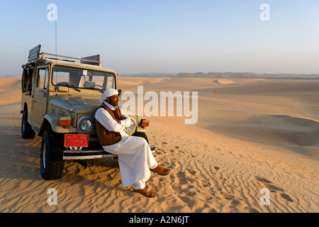 Man sitting on jeep front in desert, Siwa Oasis, Libyan Desert, Egypt Stock Photo