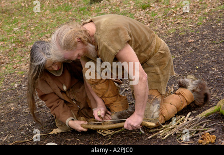 Prehistoric man & woman stone age reenactors trying to make fire at The Museum of Welsh Life St Fagans Cardiff Wales UK Stock Photo
