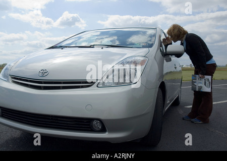 YOUNG WOMAN LOOKING AT 2004 TOYOTA PRIUS GASOLINE-ELECTRIC HYBRID CAR Stock Photo