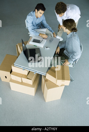 Three male colleagues grouped around cell phone on desk, surrounded by cardboard boxes Stock Photo