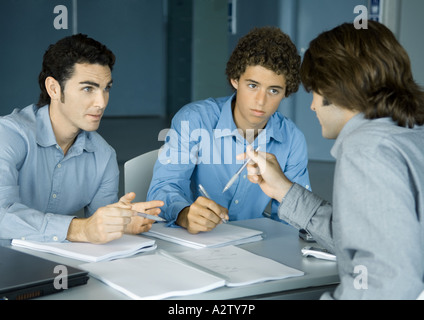 Three male colleagues sitting at table talking about documents Stock Photo
