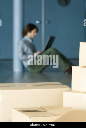 Young man sitting on floor using laptop, cardboard boxes in foreground Stock Photo