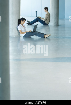 Young woman and man sitting on floor, using laptops Stock Photo