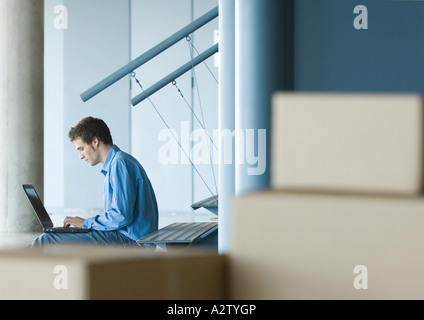 Man sitting on stairs using laptop, cardboard boxes in foreground Stock Photo