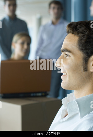 Young man smiling, profile, colleagues using laptop in background Stock Photo