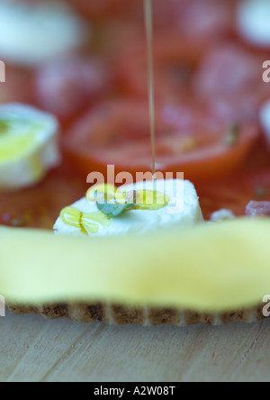 Olive oil being drizzled on uncooked tomato, goat cheese and ham tart Stock Photo