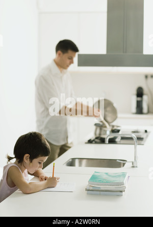 Child doing homework on kitchen counter while father cooks Stock Photo