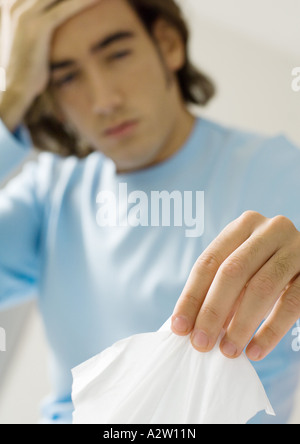 Young man holding head and taking facial tissue Stock Photo