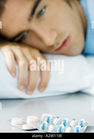 Man lying down, looking at packs of pills Stock Photo