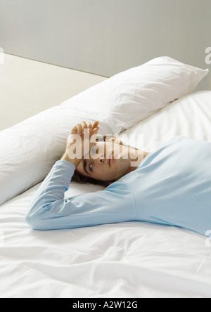 Man lying on bed with hand on forehead Stock Photo