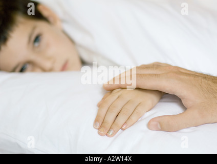 Child lying in bed, father's hand on child's Stock Photo