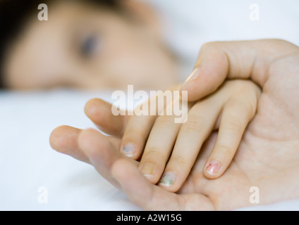 Child lying in bed, father's hand holding child's Stock Photo