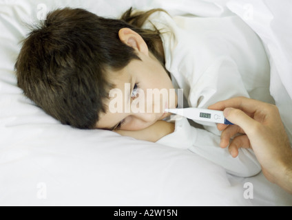 Child lying in bed, having temperature taken Stock Photo