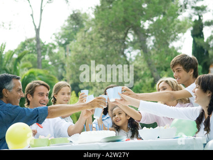 Outdoor birthday party attended by multi-generational family, everyone clinking cups Stock Photo
