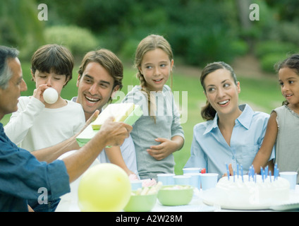 Outdoor birthday party, mature man handing girl presents Stock Photo