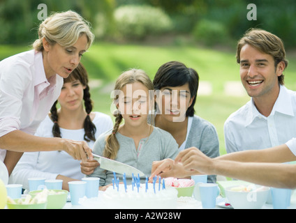 Outdoor birthday party, mature woman cutting birthday cake Stock Photo