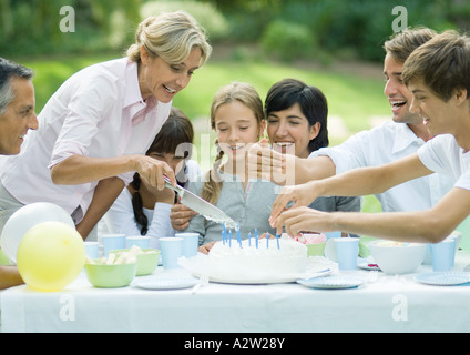 Outdoor birthday party, mature woman cutting birthday cake Stock Photo