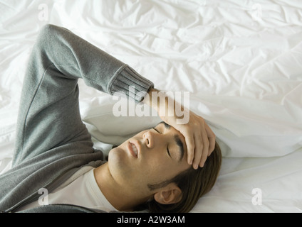 Man lying on bed, holding head Stock Photo