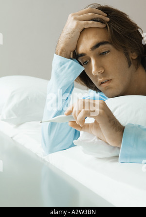 Man lying in bed, looking at thermometer Stock Photo