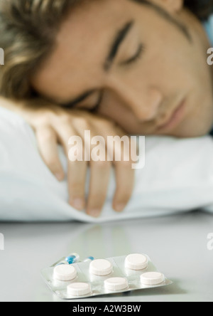 Man lying in bed, pack of pills in foreground Stock Photo