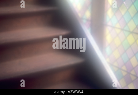 Atmospheric detail of wooden stairs rising past part of a multicoloured diamond leaded paned window Stock Photo