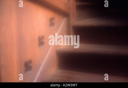 Atmospheric detail of a turn in a wooden staircase with a panel on one side with quatrefoil cutouts Stock Photo