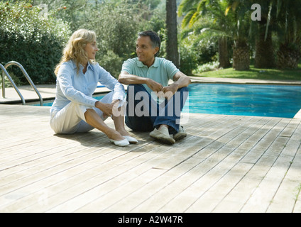 Mature couple sitting on deck by swimming pool Stock Photo