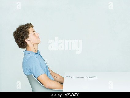 Young man sitting at table, listening to portable MP3 player Stock Photo