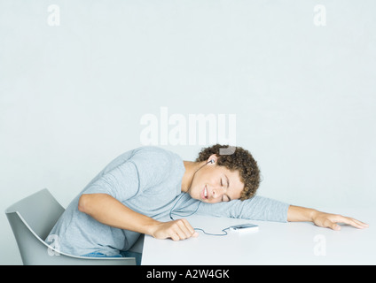 Young man sitting with head on table, listening to portable MP3 player Stock Photo