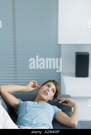 Woman lying on sofa, putting in earphones Stock Photo