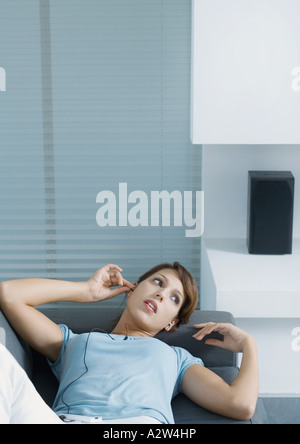 Woman lying on sofa, putting in earphones