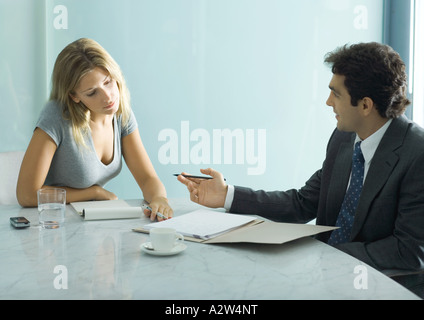 Professional man and woman speaking and looking over document at table Stock Photo