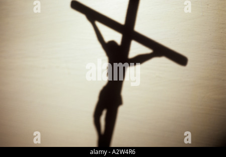 A shadow or silhouette against a pale wall of Jesus Christ hanging from a crucifix viewed from behind Stock Photo