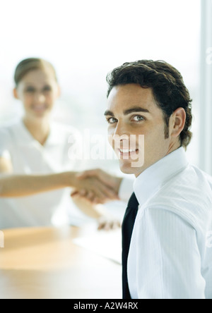 Man and woman shaking hands across table, man smiling over shoulder at camera Stock Photo