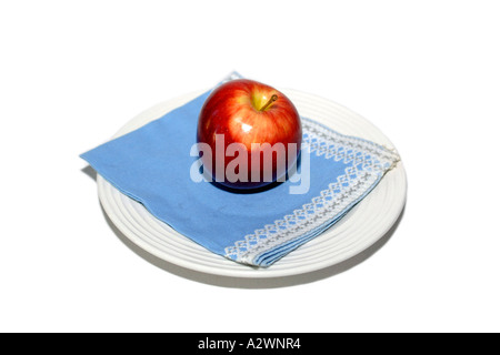 A bright polished Red Apple sitting on a blue napkin on a white plate Stock Photo