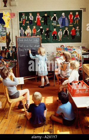 Group of young school children in classroom. Girl writing with chalk on blackboard during lesson. Stock Photo