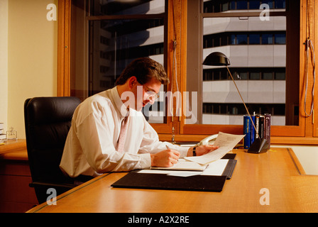 Man seated writing at desk working in office. Stock Photo