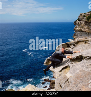 Concept. Business man in suit climbing a cliff with view of the ocean horizon. Stock Photo